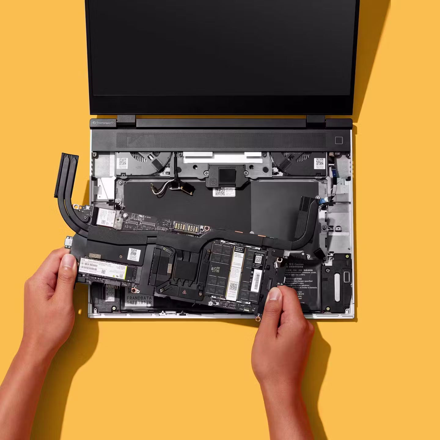 Top-down studio shot of a Framework Laptop 16 with a person installing the mainboard.