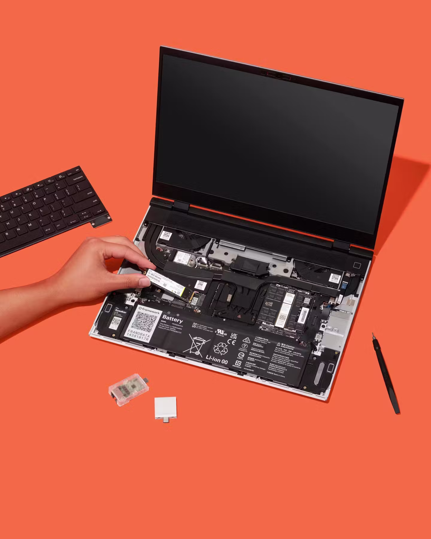 Top-down studio shot of a Framework Laptop 16 with a hand installing a component on an orange backdrop.