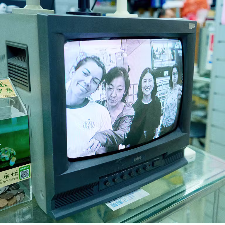 A vintage CRT television monitor sitting on a glass shelf, displaying a black-and-white photograph of four smiling Framework employees on its screen.