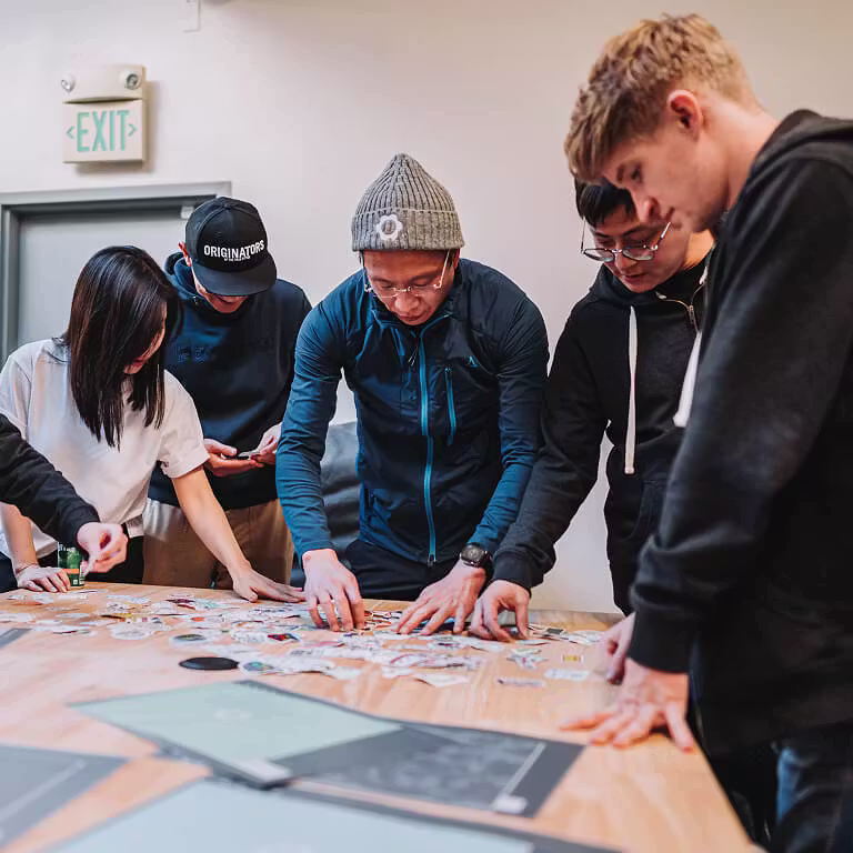 A group of employees gathered around a wooden table, looking down and sorting through a large pile of assorted stickers.