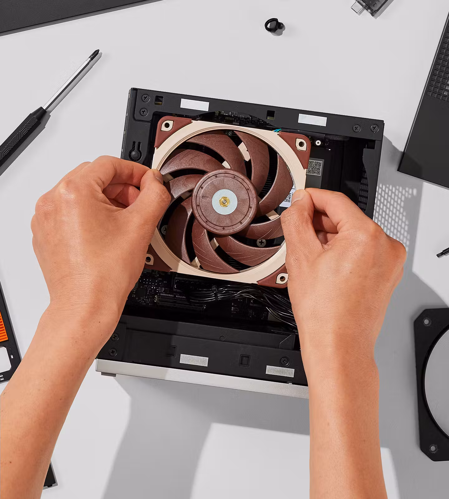 Top-down view of a person's hands installing a brown-and-beige Noctua cooling fan directly into the desktop chassis.