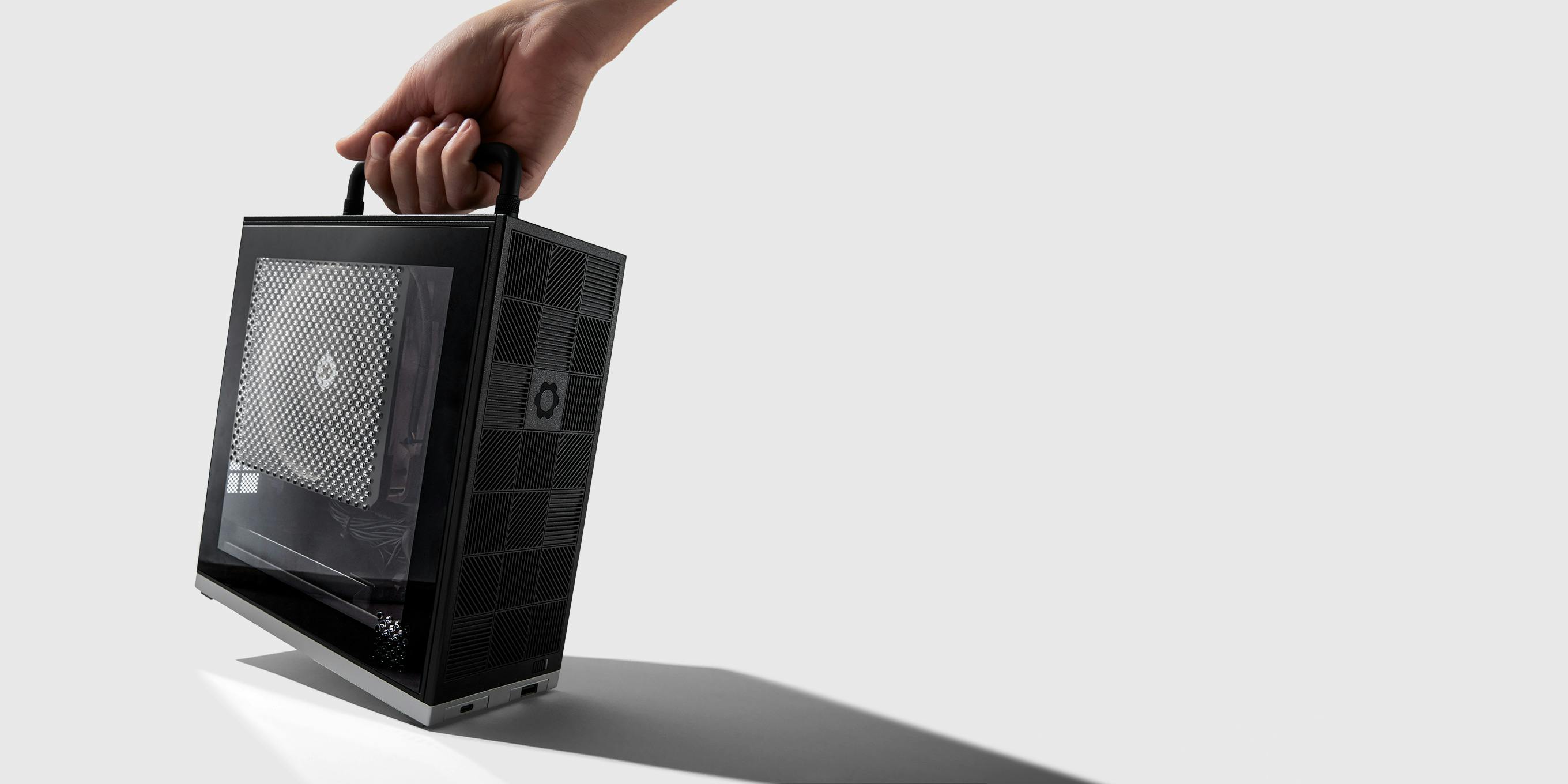 A hand lifts the Framework Desktop by its top handle.